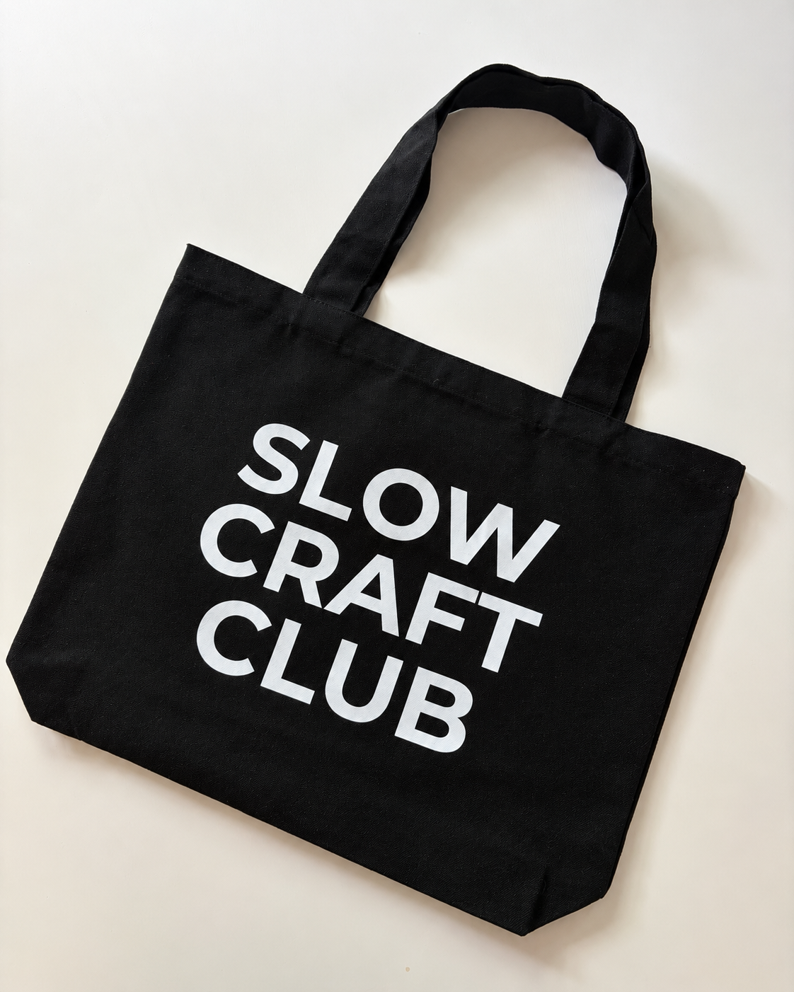 Black canvas tote bag with white “Slow Craft Club” lettering and shoulder handles
