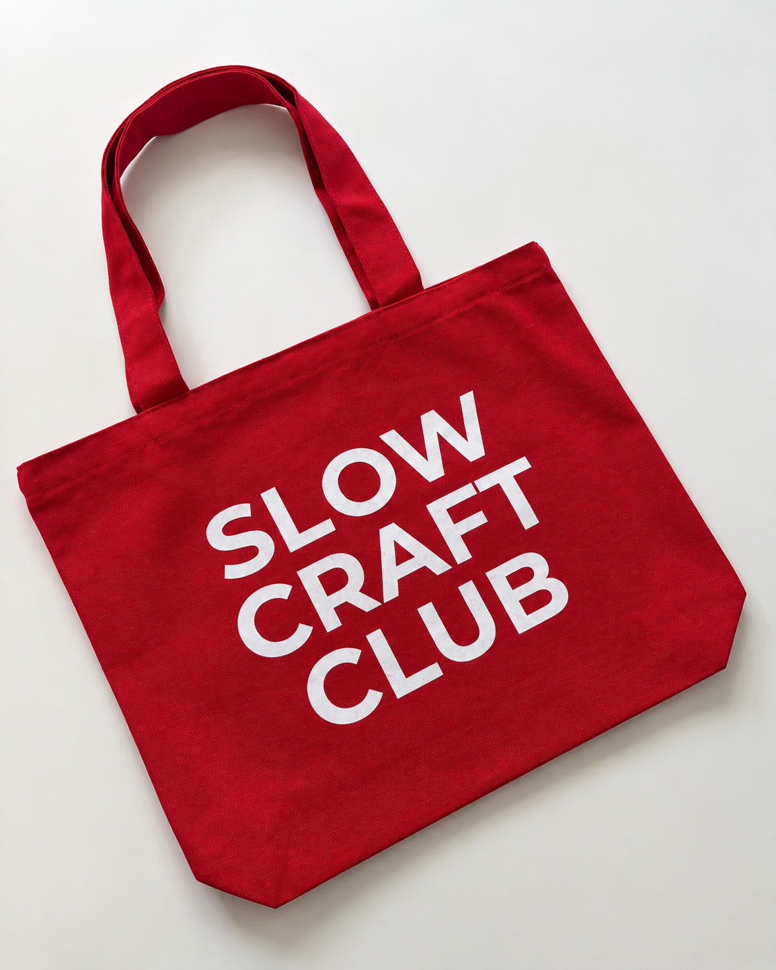 Red canvas tote bag with white “Slow Craft Club” lettering and shoulder handles
