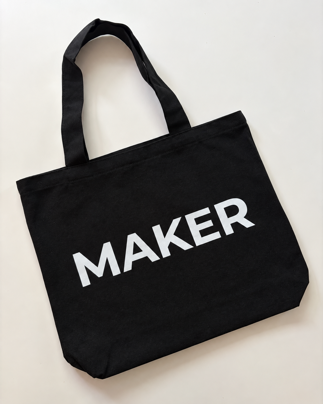 Black canvas tote bag with white “Maker” lettering and shoulder handles