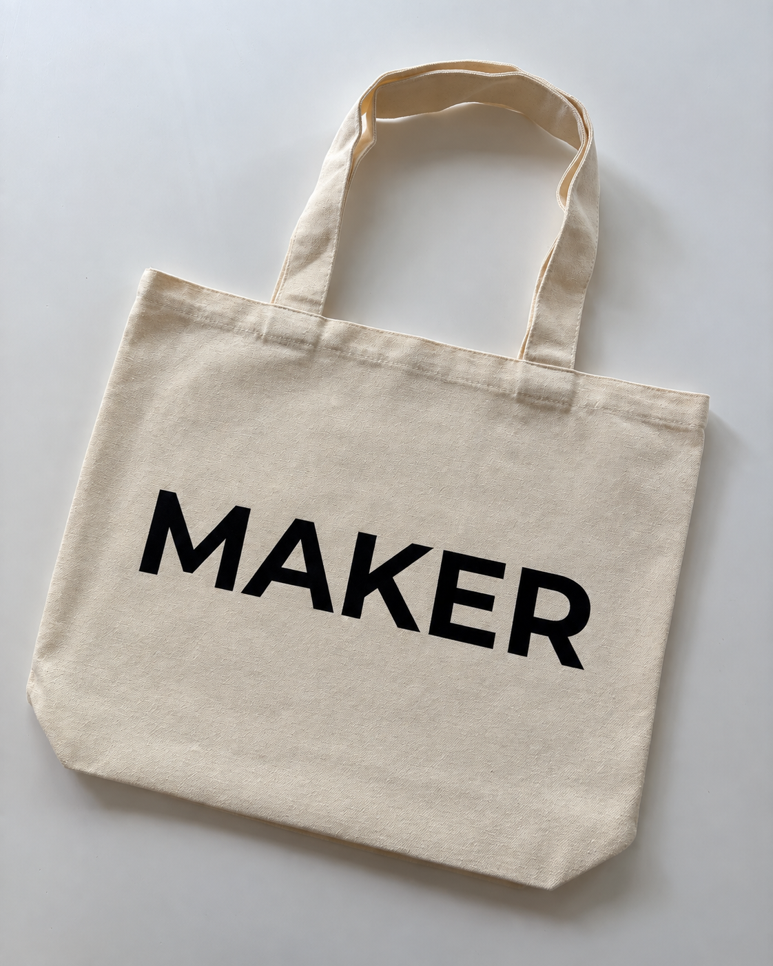 Cream canvas tote bag with black “Maker” lettering and shoulder handles