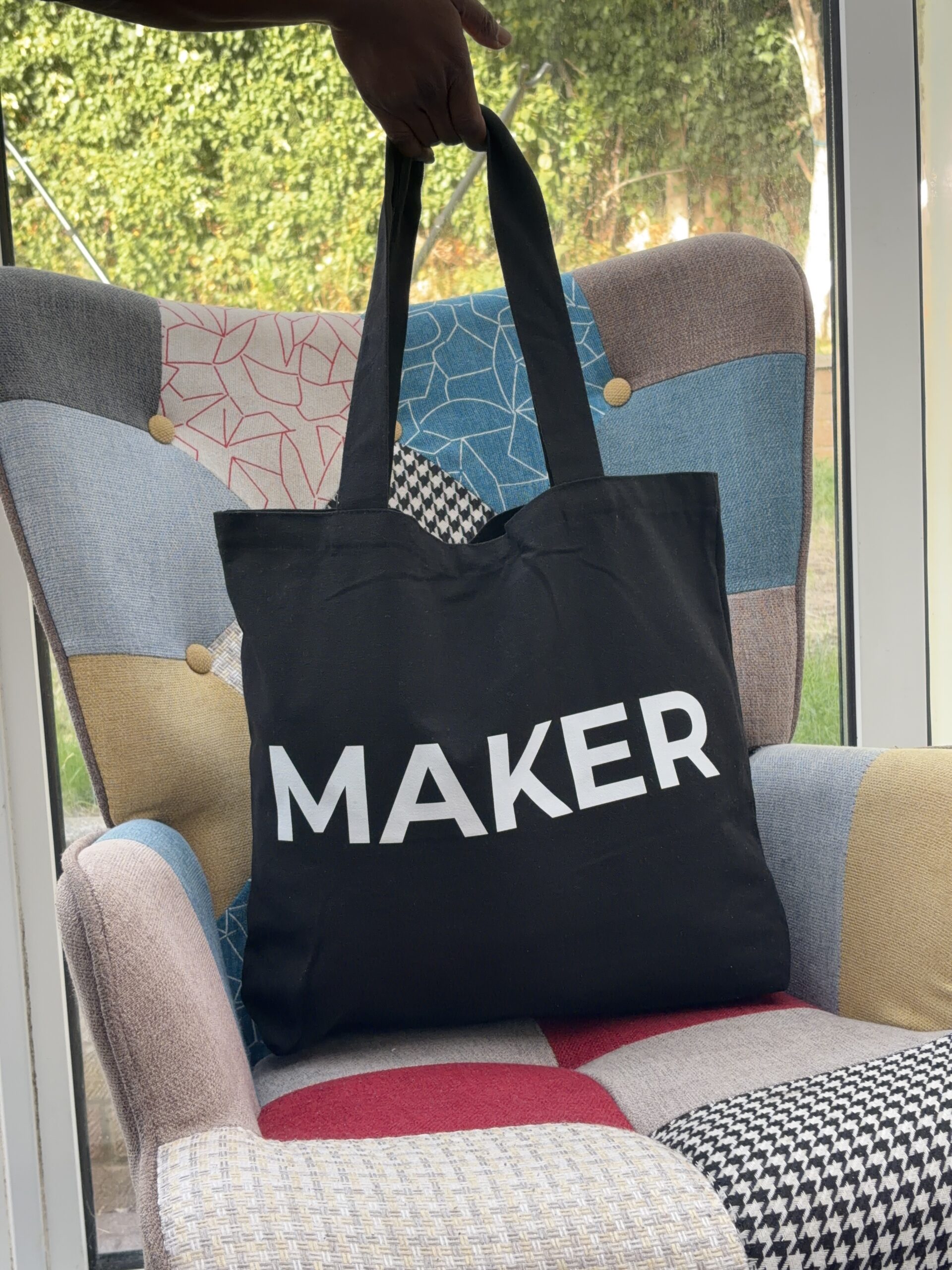 Black canvas tote bag with white “Maker” lettering and shoulder handles