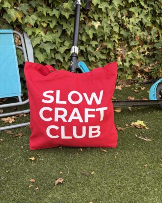 Red canvas tote bag with white “Slow Craft Club” lettering.