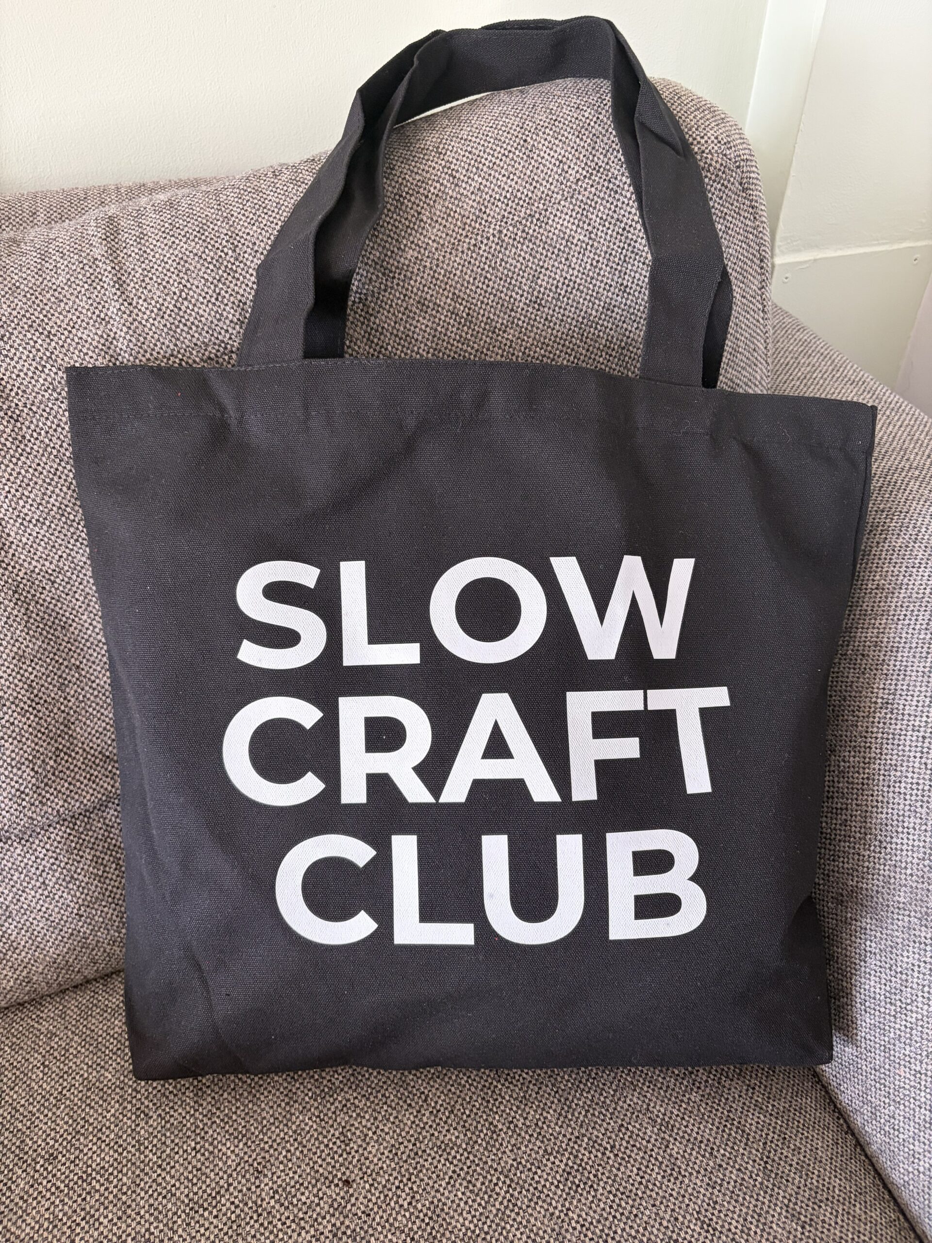 Black canvas tote bag with white “Slow Craft Club” lettering and shoulder handles